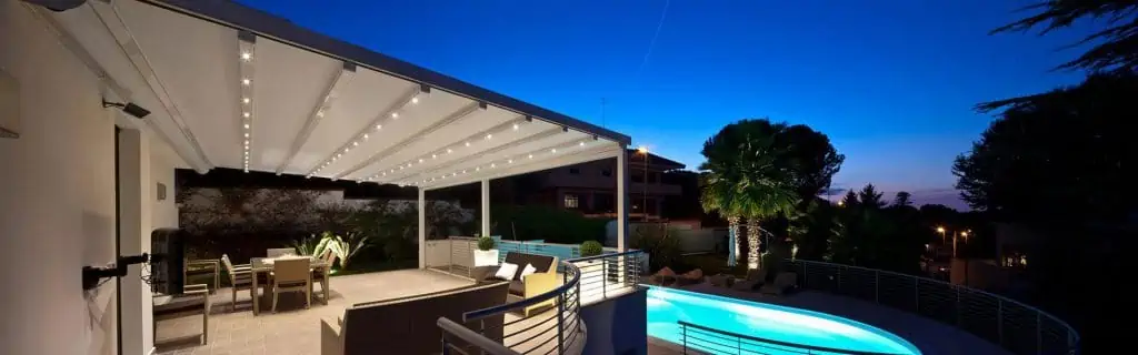 Pergola with a retractable roof over a poolside patio at dusk